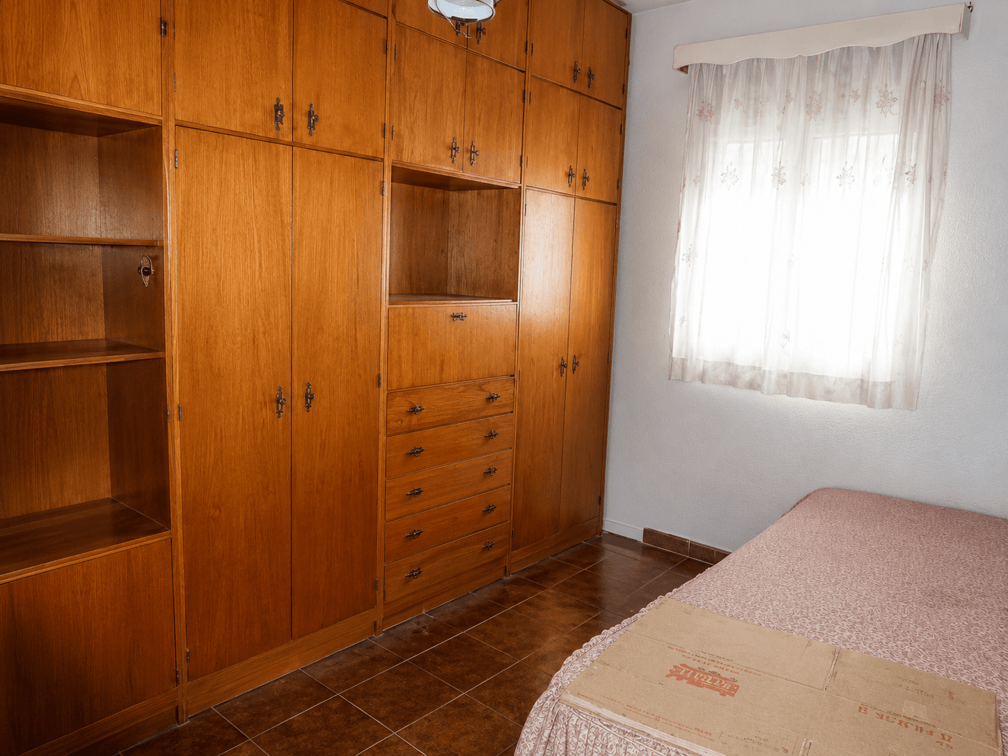 Dormitorio antes de la reforma, con armario de obra en madera y suelo de baldosa