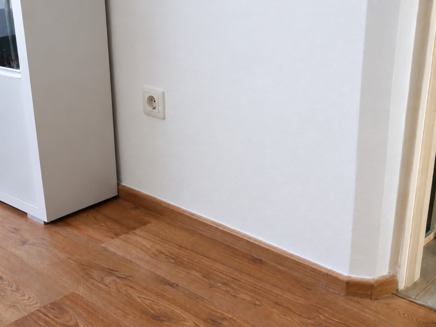 La misma pared después de reparar la humedad, con pintura lisa y rodapié repuesto